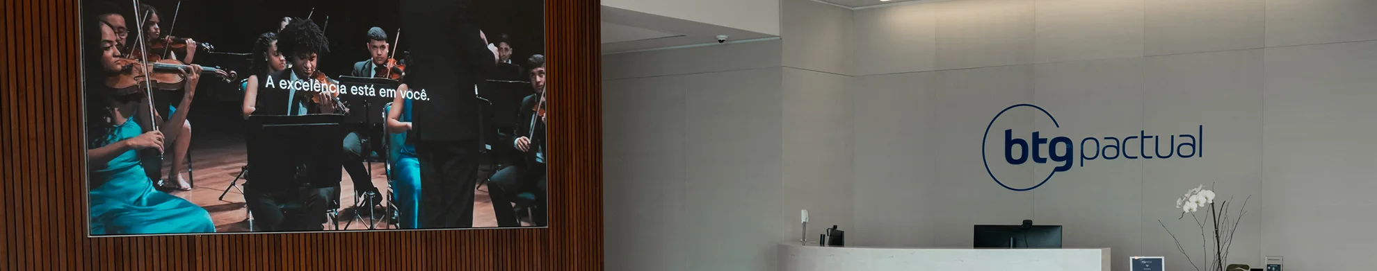 Sala com tela de reprodução e logo do BTG Pactual ao fundo